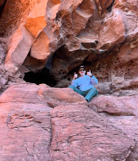 man giving 2 thumbs up posing in front of cave