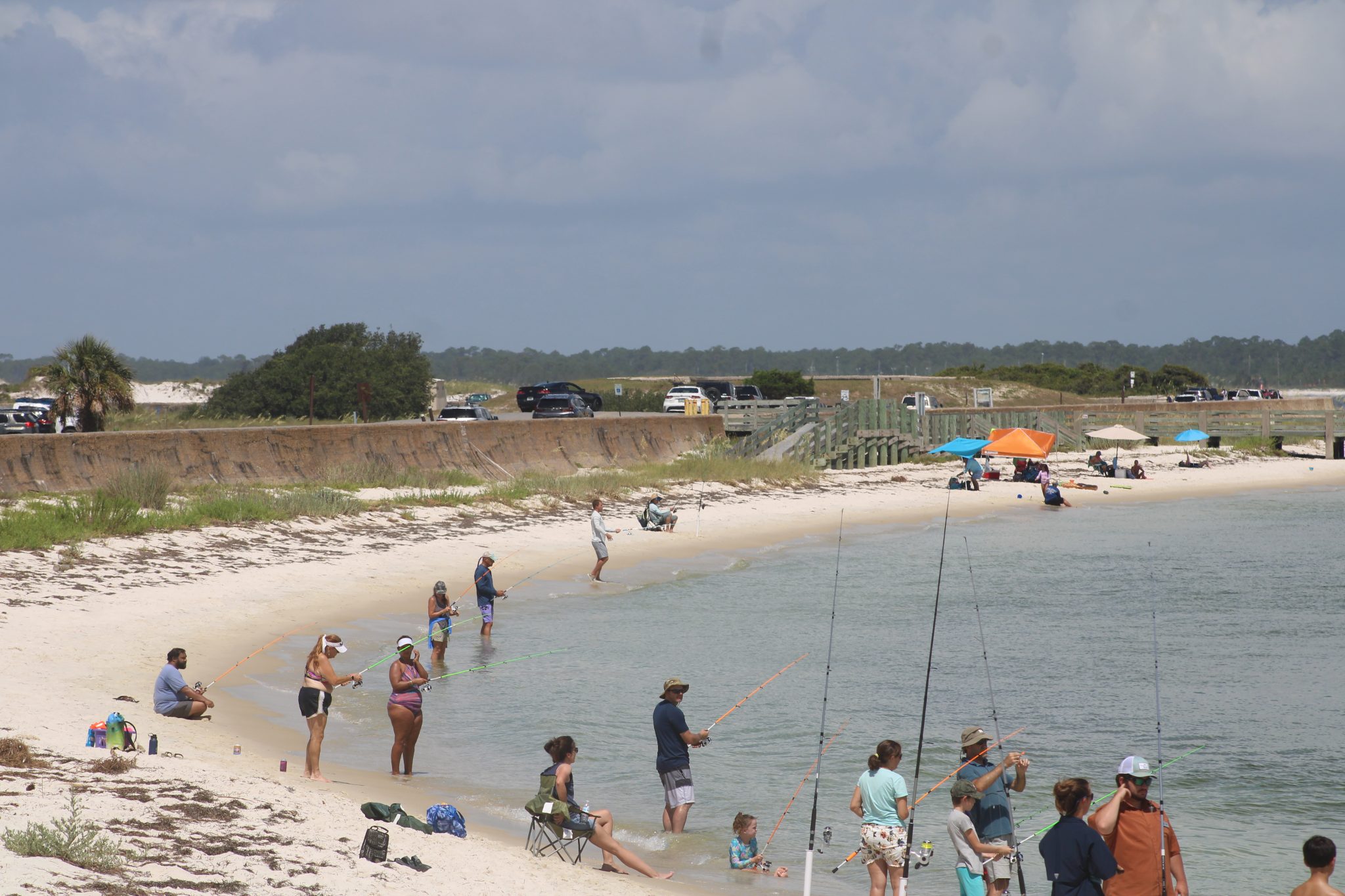 A beach at Fork Pickens. Many people are holding fishing poles. The seawall is visible in the background.