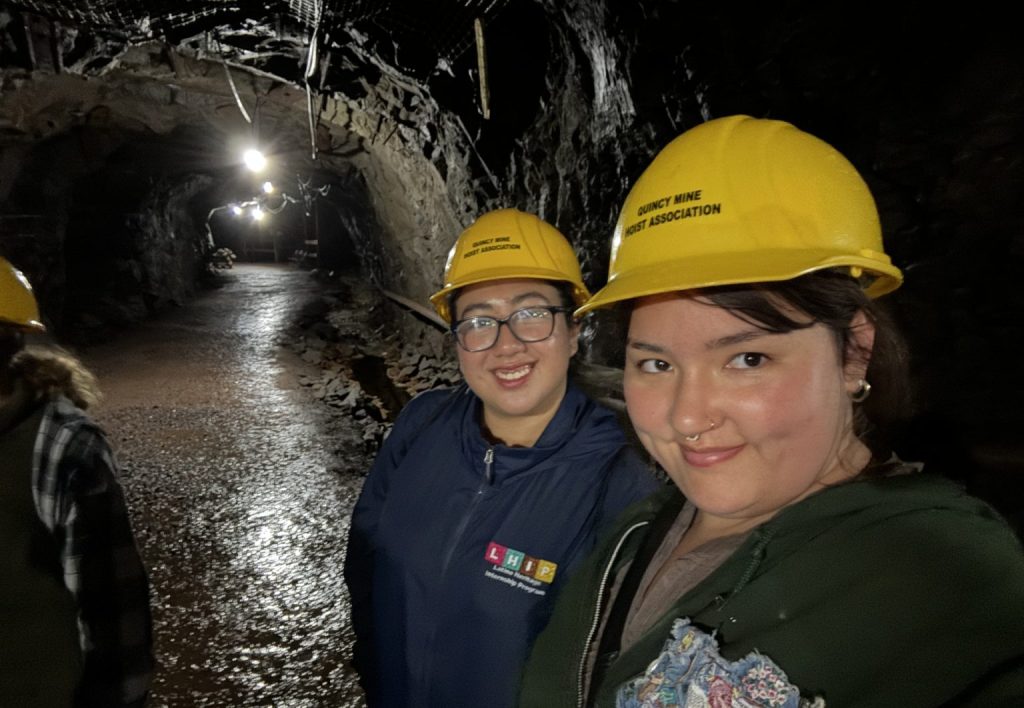 Emily Wright, a Fish and Feathers intern, and her intern roommate are standing in a cave, both wearing yellow caving hard hats.