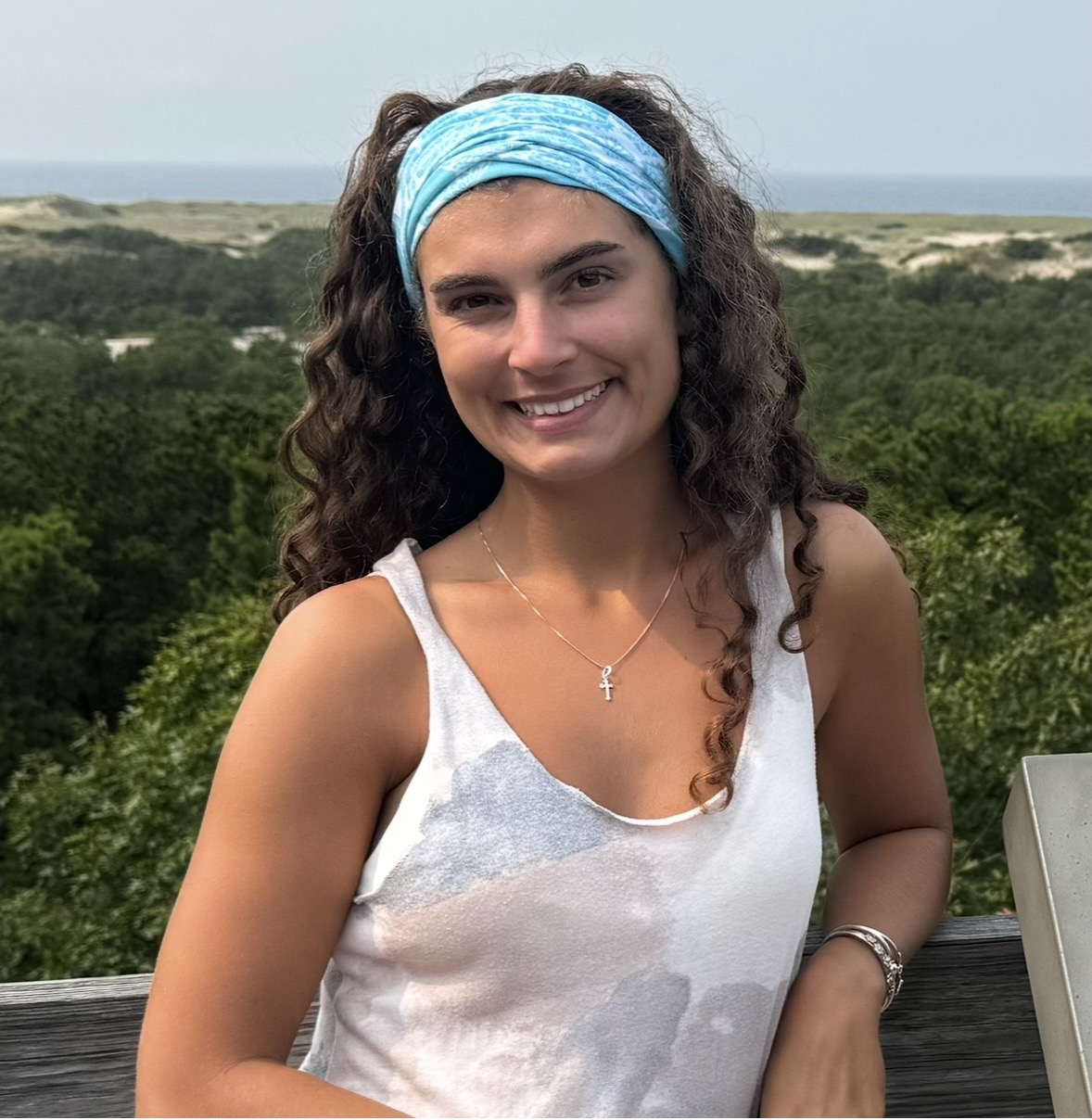 Sarah standing outside on an observation deck with green trees and the ocean behind her.