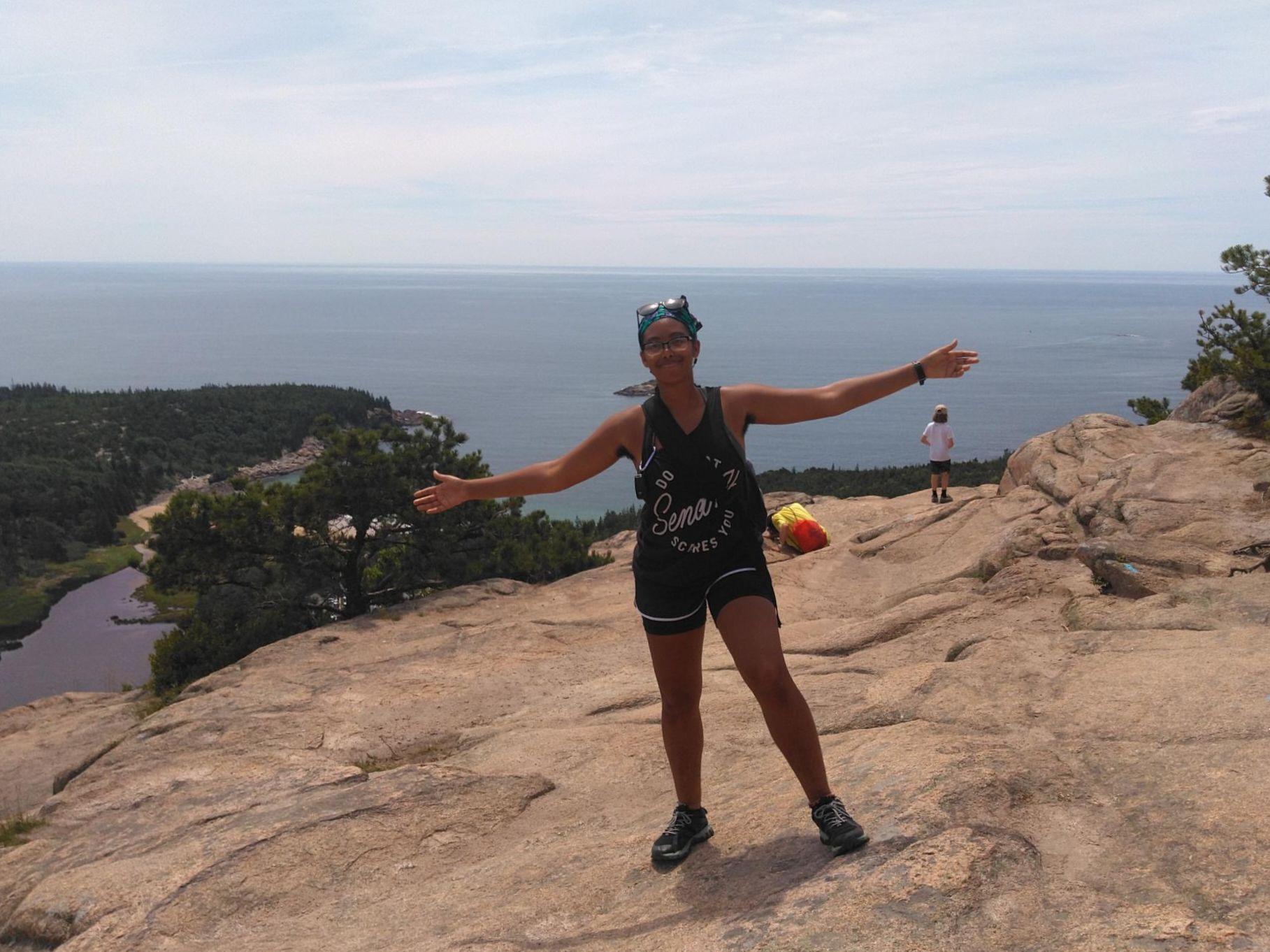 A person standing on top of a bare mountain with arms outstretched. In the background