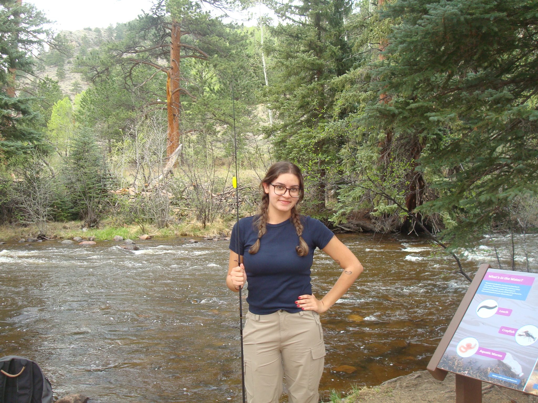 Dhara is standing holding a fishing rod in front of a river.