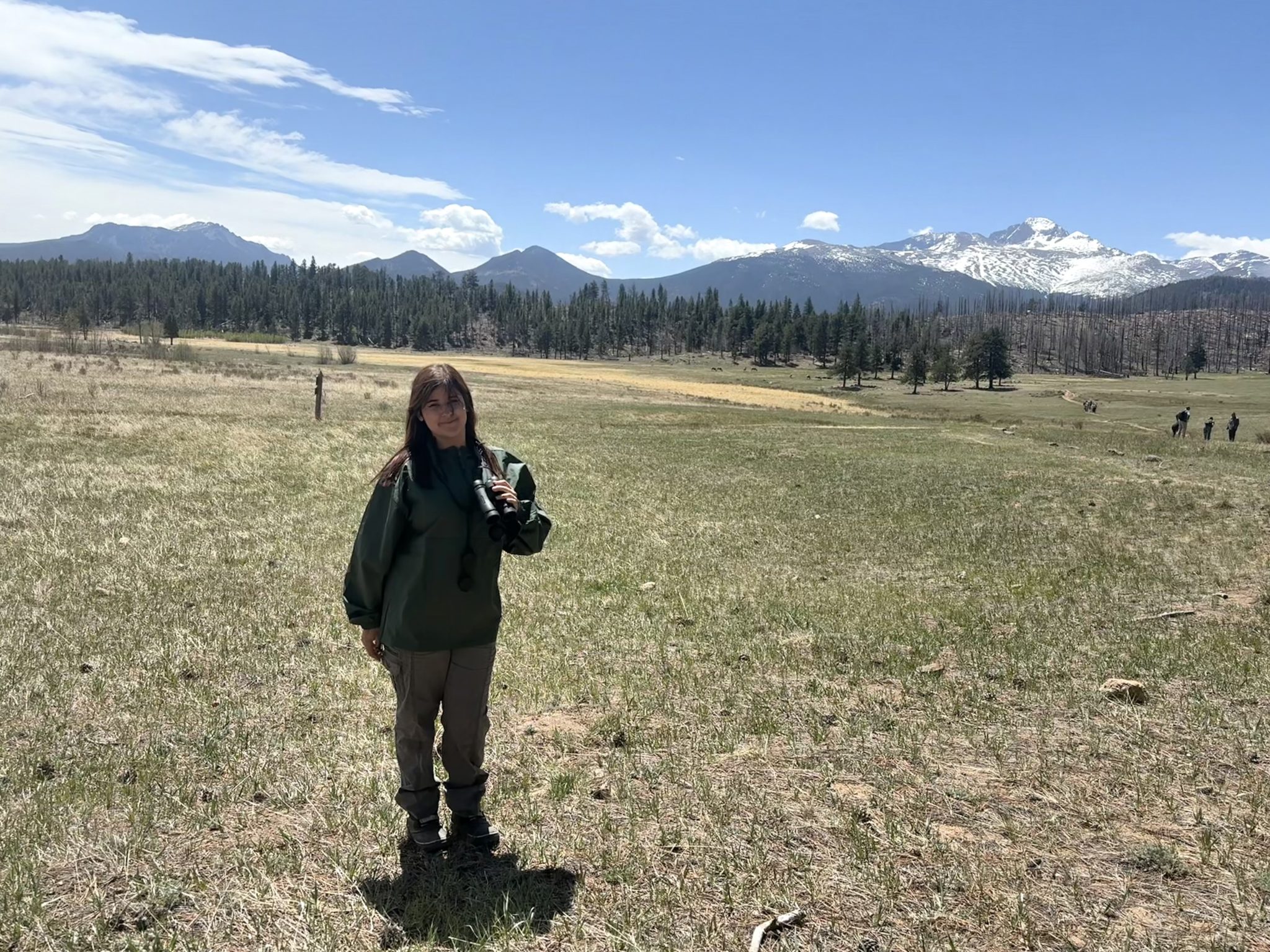 Picture of Genevieve holding binoculars in front of Rocky Mountains.