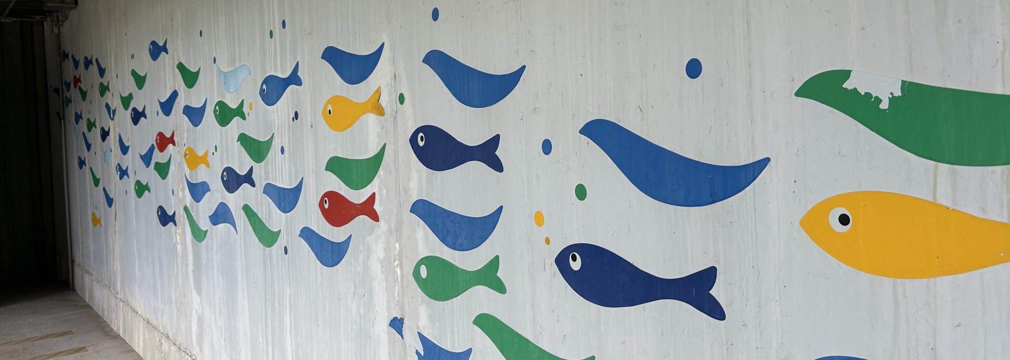 Picture of a wall with a painted mural containing many colorful fish swimming.