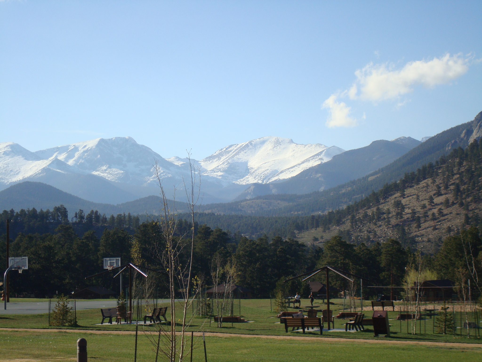 A picture of the skyline in Estes Park, Colorado. There are snow-covered mountains in the back and trees and benches in the foreground.